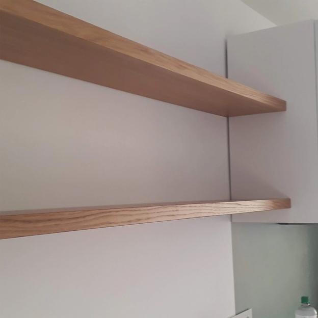Zwei identische weiße Zimmertüren mit Kassettenoptik und schwarzen Türgriffen nebeneinander. Zwei schlichte Wandregale aus Holz, elegant in einer modernen Küche integriert.