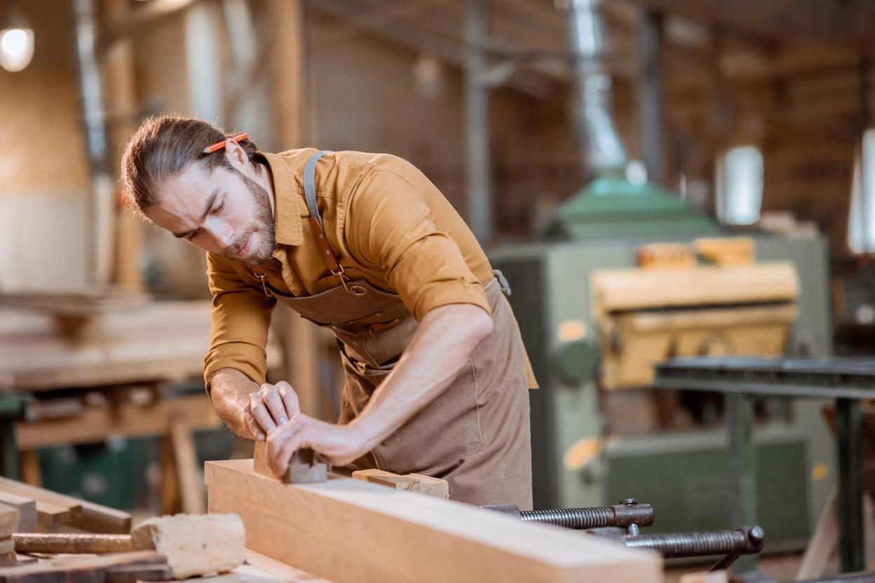 Schreiner arbeitet konzentriert mit einem Hobel an einem Holzstück in einer Werkstatt.
