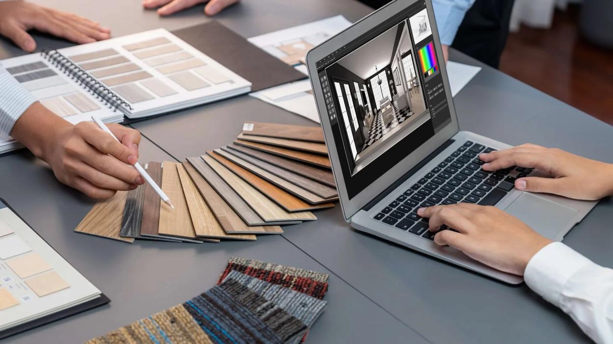 Besprechungstisch mit Farbmustern, Farbpaletten und einem Laptop, auf dem ein Innenraum-Layout angezeigt wird.