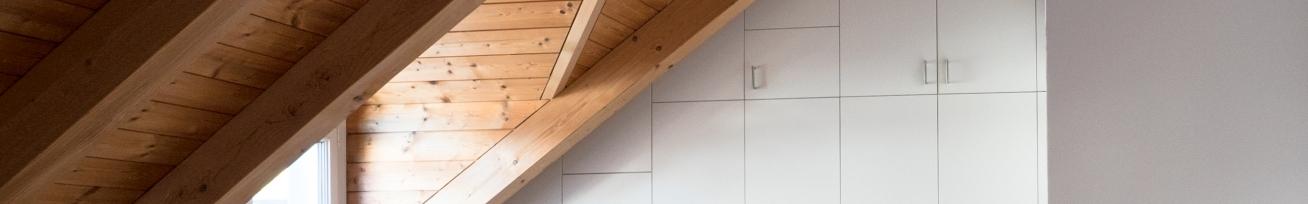 Nischenlösung für Einbauschrank an holzbelassener Dachschräge Nischenlösung für weißen Einbauschrank mit Schubladen und Türen an in dunklem Holz belassener Dachschräge