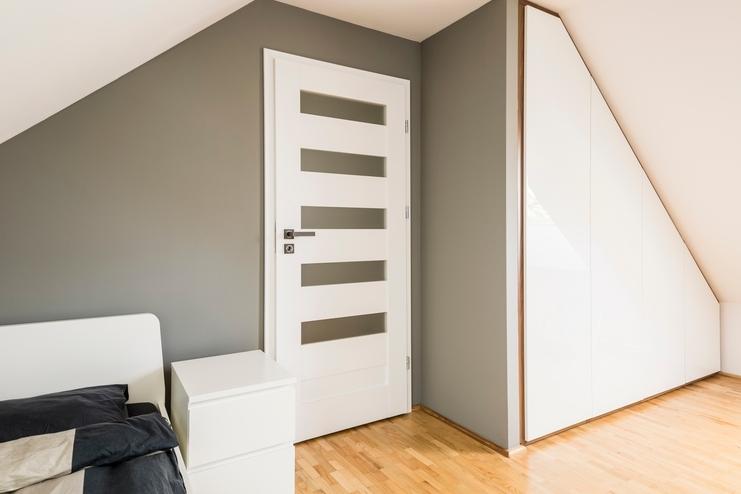 Weißer Einbauschrank an Dachschräge Weißer Einbauschrank an Dachschräge, dreieckig mit Trennwand zur Zimmertür an hellem Parkett.